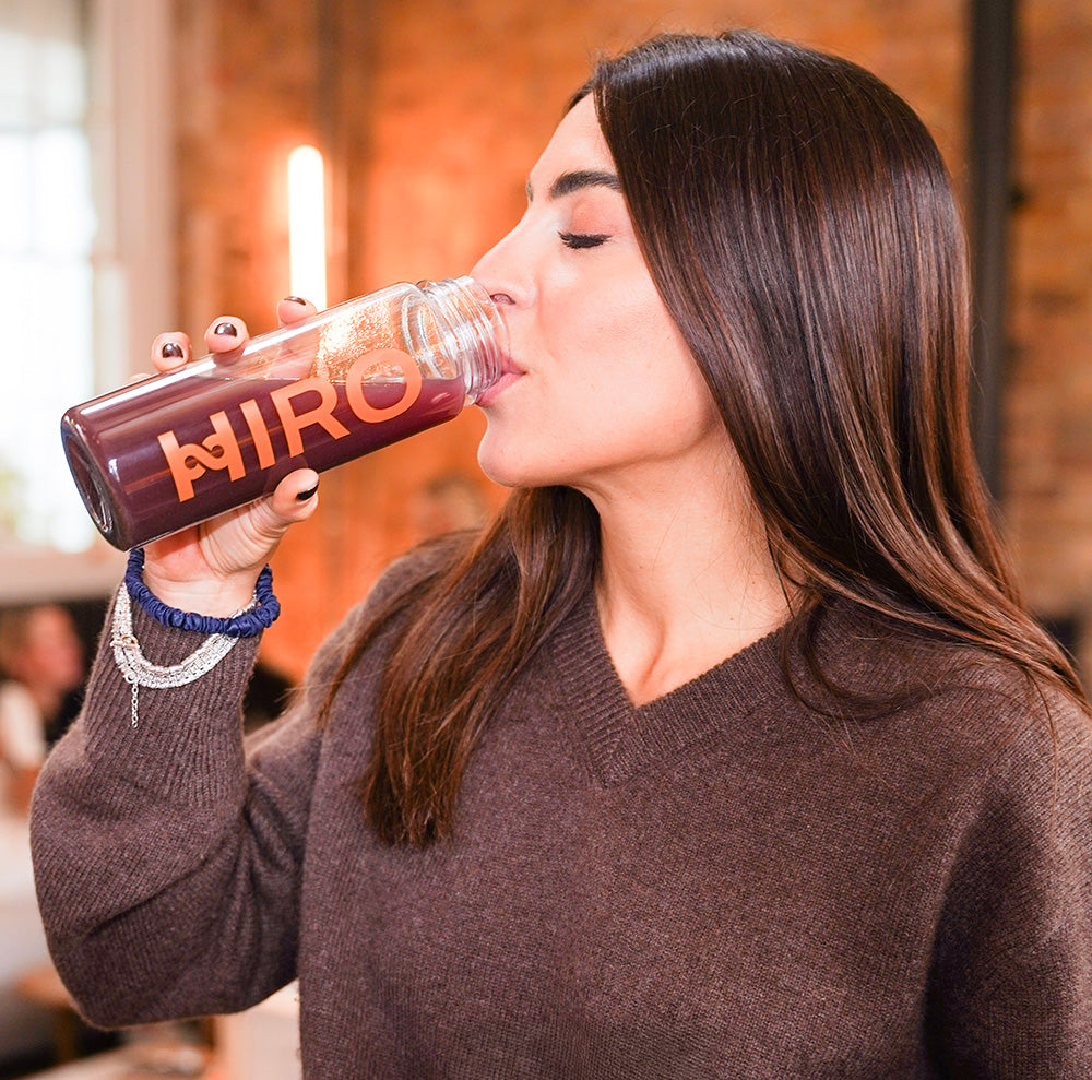 Woman drinking from a bottle labeled 'HIRO' in an indoor setting.